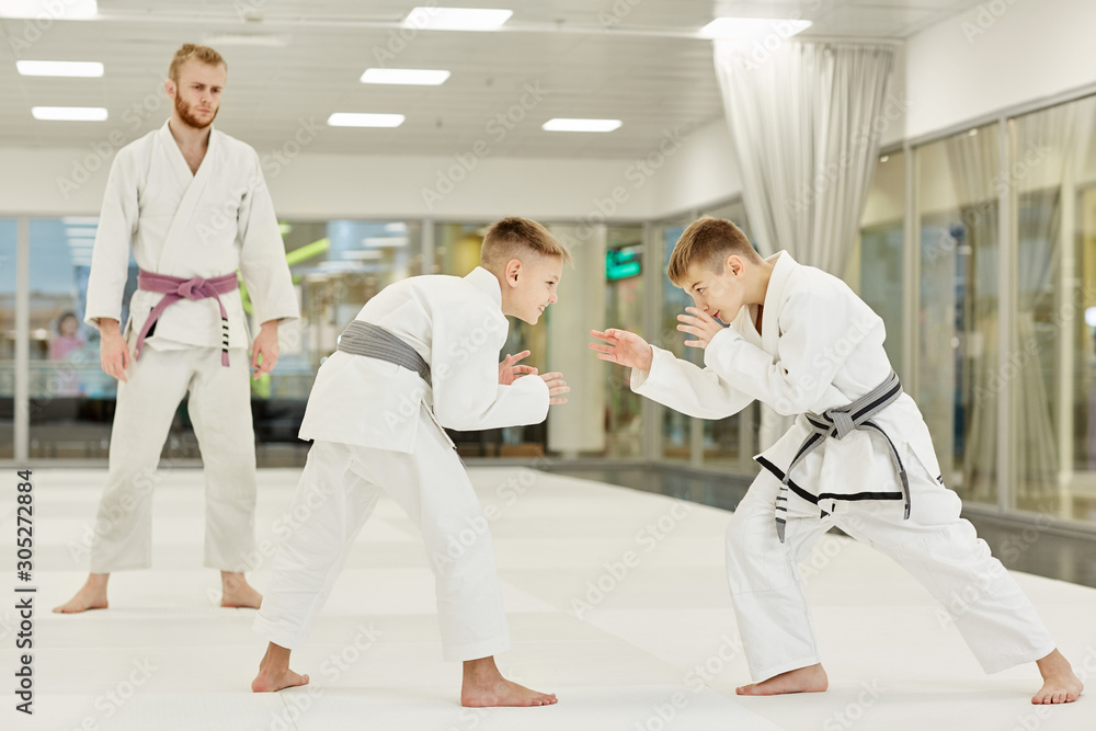 Obraz premium Two boys in kimono learning to fight during training in karate while their coach standing and watching for them