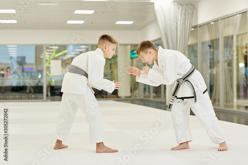Two young judoists in kimono standing and fighting with each other in the gym