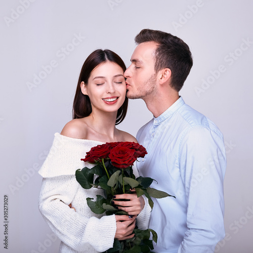 Handsome elegant guy is giving roses to his beautiful girlfriend and kissing her.