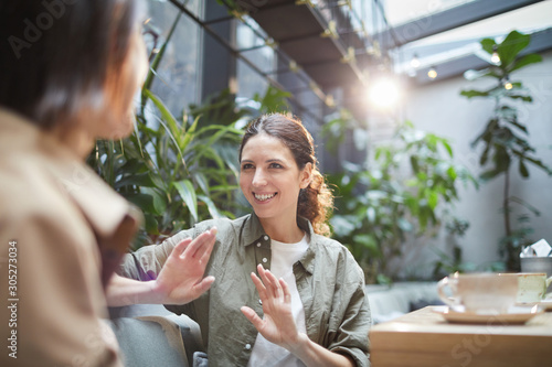 Papier peint Waist up portrait of smiling young woman talking to friend on outdoor cafe terra