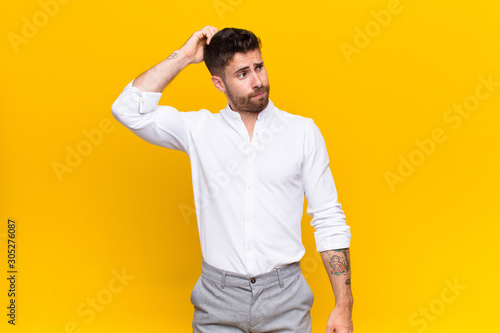 Obraz na płótnie young handosme man feeling puzzled and confused, scratching head and looking to