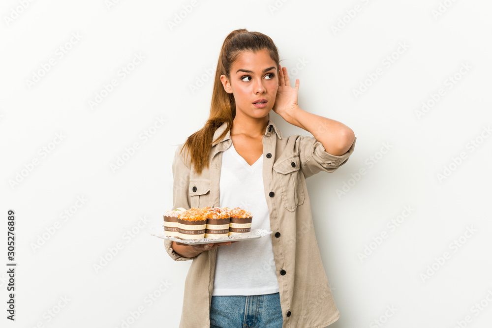 Young caucasian woman holding sweet cakes trying to listening a gossip. Young caucasian woman holding sweet cakes trying to listening a gossip.