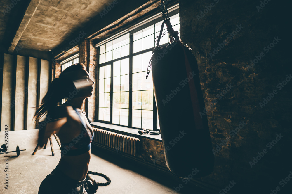 Attractive woman training with punching a bag with gloves in the gym. Sport, fitness, lifestyle concept.