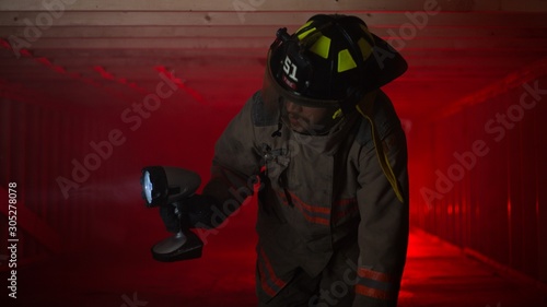 Fototapeta Naklejka Na Ścianę i Meble -  Fire fighter crawling in smoke filled area shining light looking for survivors