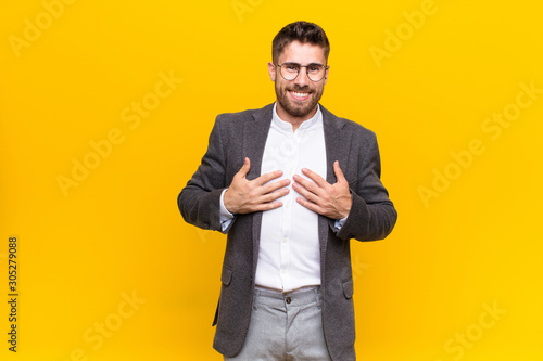 young handosme man looking happy, surprised, proud and excited, pointing to self against flat color wall photo