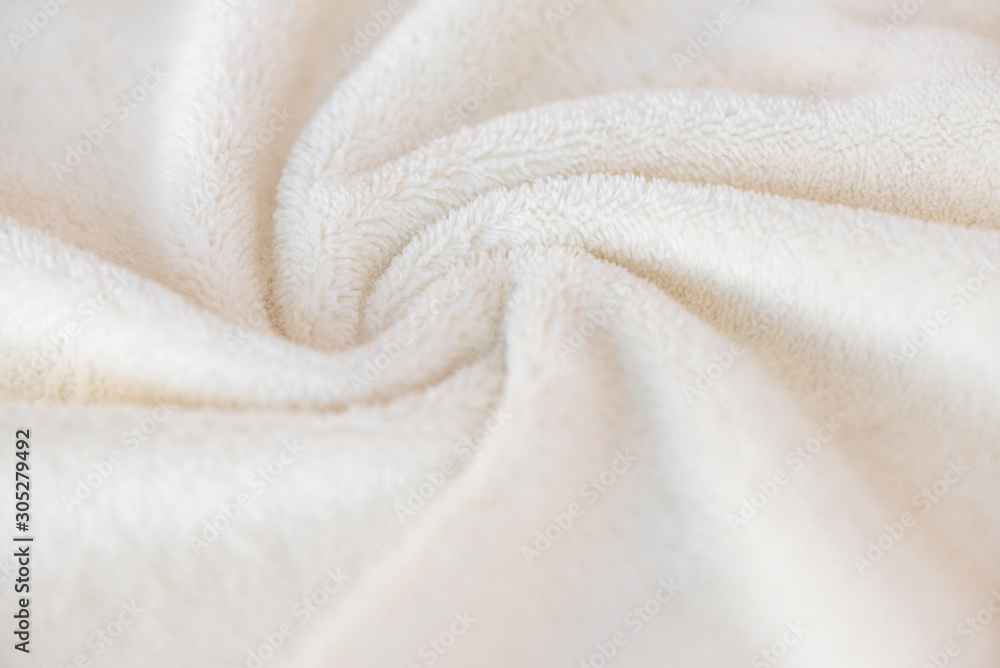 White delicate soft background of plush fabric plaid. Texture of beige soft fleecy blanket textile with twisted folds