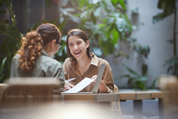 Portrait of cheerful young woman talking to friend or colleague during business meeting on outdoor cafe terrace, copy space