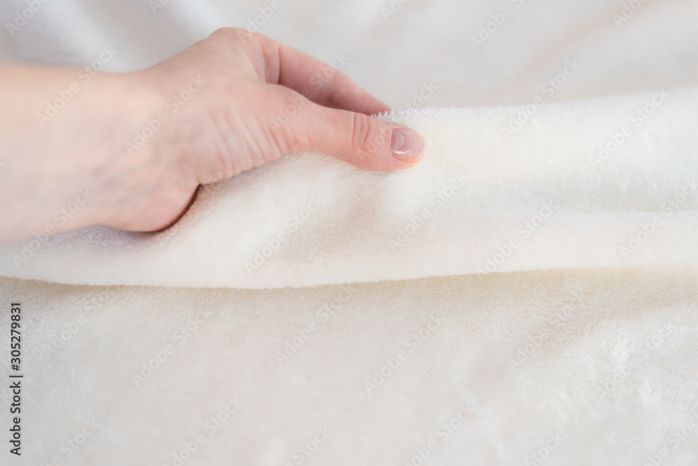 Female hand touches soft cozy plaid of white fabric with a pile. Textile material, pleasant to the touch Female hand touches soft cozy plaid of white fabric with a pile. Textile material, pleasant to the touch