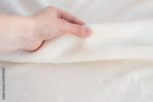Female hand touches soft cozy plaid of white fabric with a pile. Textile material, pleasant to the touch