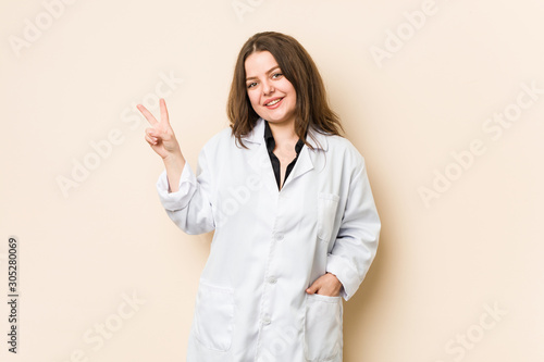 Young doctor woman joyful and carefree showing a peace symbol with fingers.