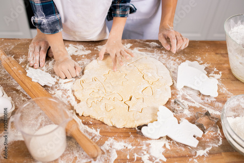 Hands of mother and son cutting figures in rolled dough while making cookies