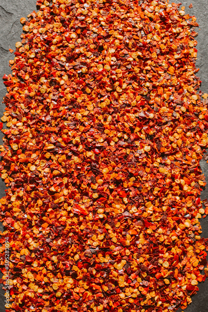 Close up view of red chili flakes on black slate background. Crushed red cayenne pepper. Close up view of red chili flakes on black slate background. Crushed red cayenne pepper.