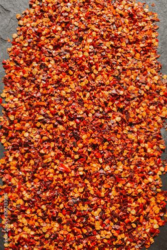 Close up view of red chili flakes on black slate background. Crushed red cayenne pepper.  © nachomp82