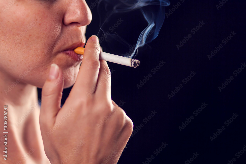 Obraz premium Woman smokes cigarette on black background. Nicotine addiction concept
