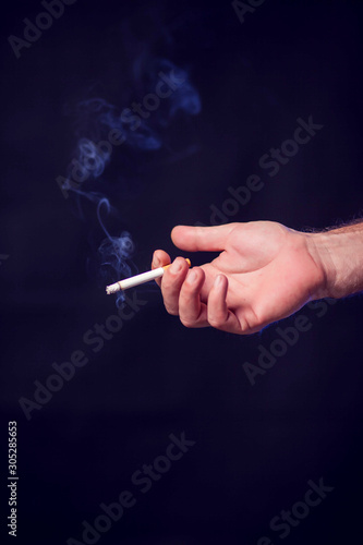 Cigarette in hand on black background. Nicotine addiction concept