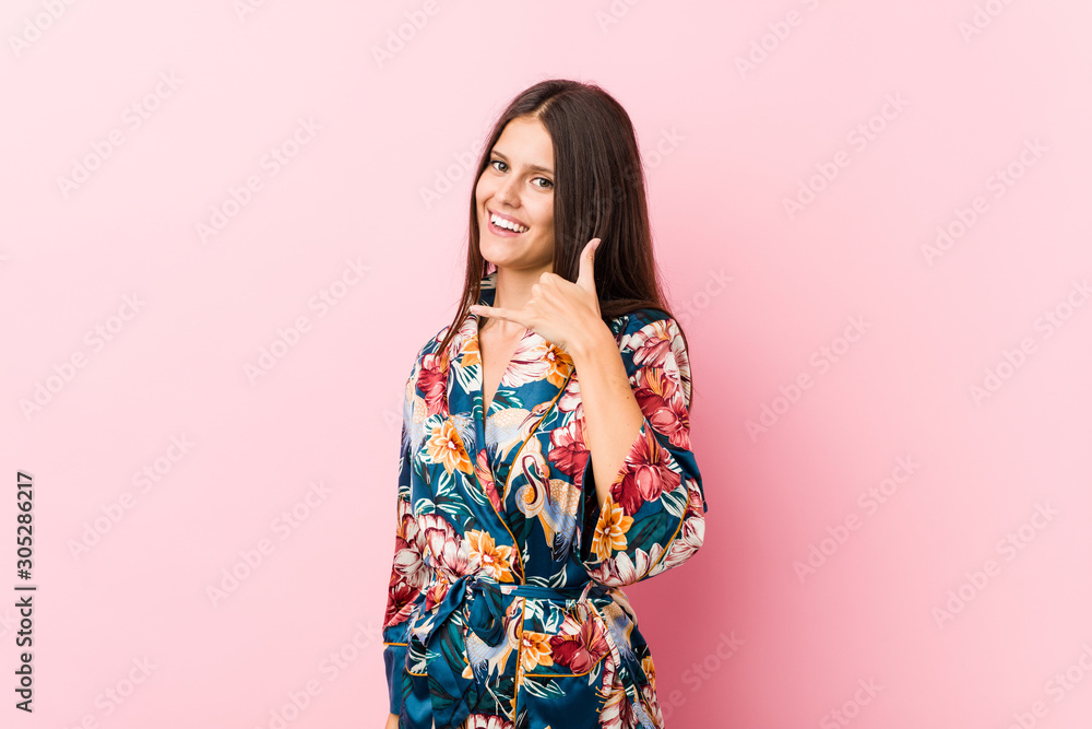 Young caucasian woman wearing a kimono pajama showing a mobile phone call gesture with fingers. Young caucasian woman wearing a kimono pajama showing a mobile phone call gesture with fingers.