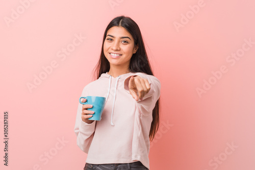 Young arab woman holding a cup cheerful smiles pointing to front.