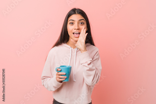 Young arab woman holding a cup shouting excited to front.