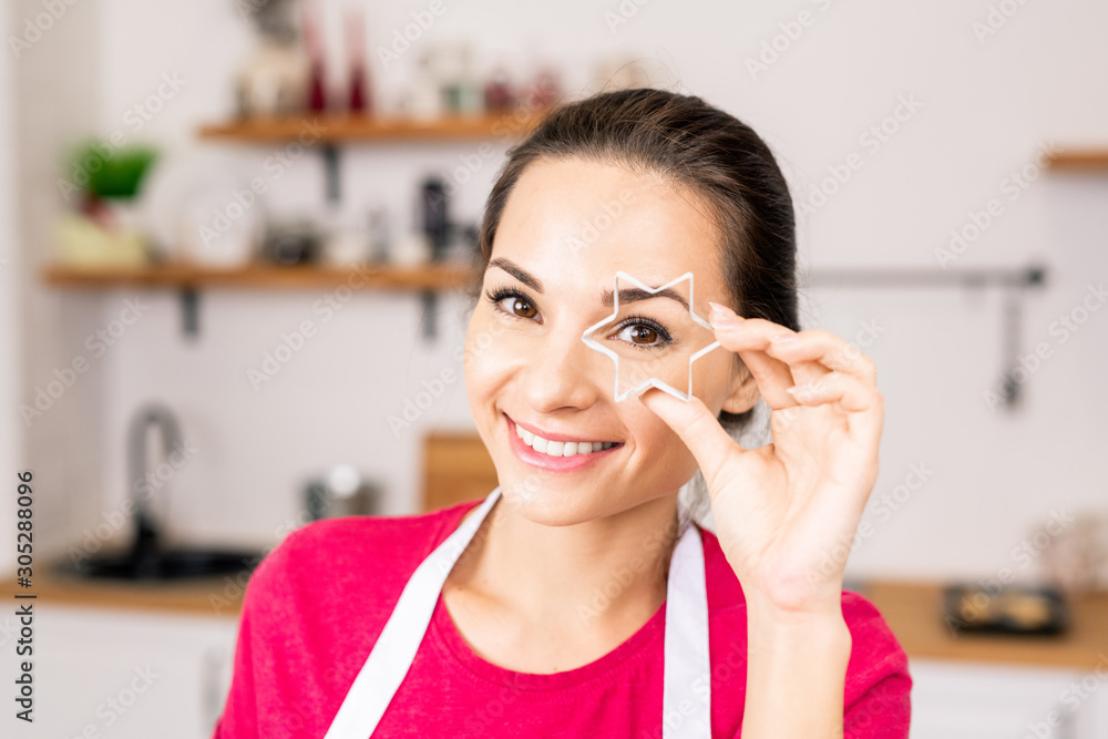Young smiling woman holding star shaped cutter for homemade cookies by face Young smiling woman holding star shaped cutter for homemade cookies by face