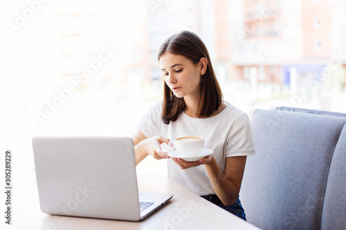 Beautiful happy woman working on laptop computer during coffee break in cafe bar