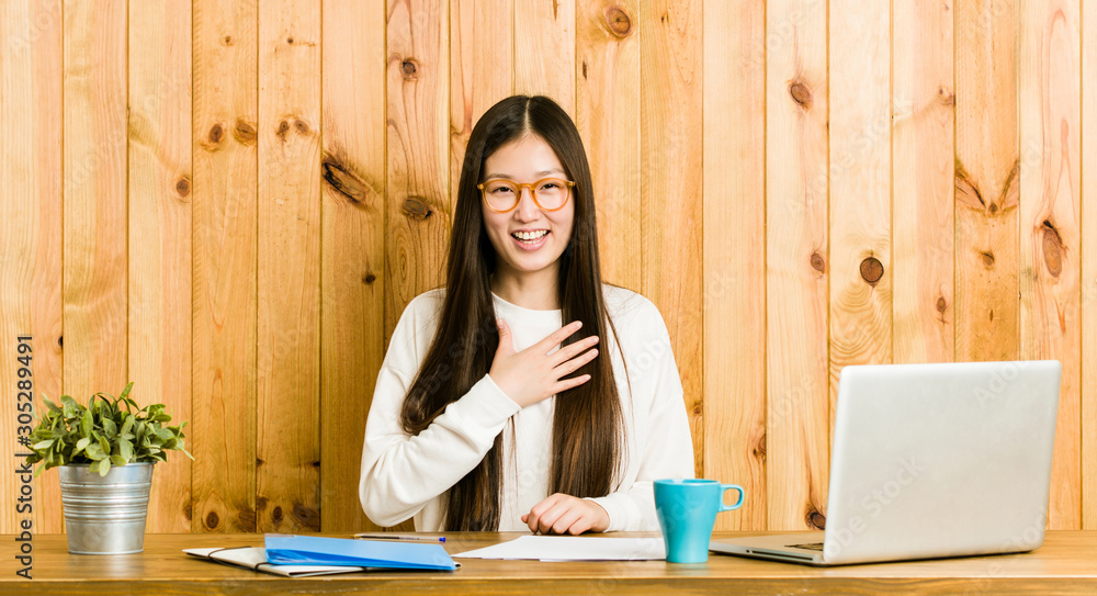 Young chinese woman studying on her desk laughs out loudly keeping hand on chest. Young chinese woman studying on her desk laughs out loudly keeping hand on chest.