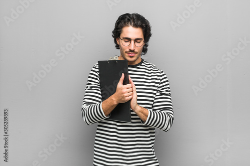 Young employee man holding an inventory holding hands in pray near mouth, feels confident. photo