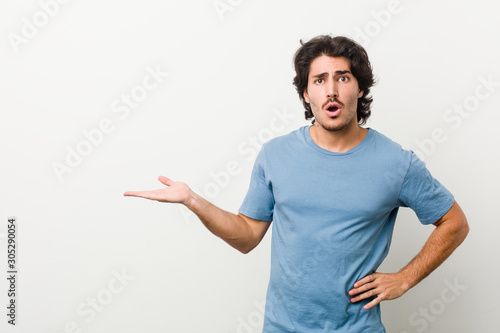 Young handsome man against a white background impressed holding copy space on palm.