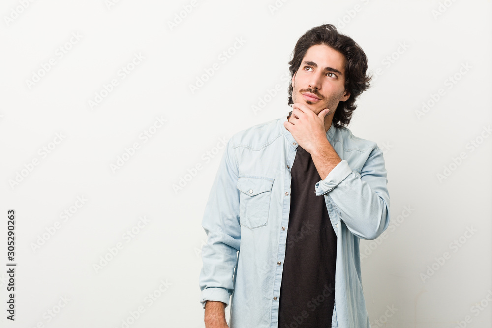 Young handsome man against a white background looking sideways with doubtful and skeptical expression. Young handsome man against a white background looking sideways with doubtful and skeptical expression.