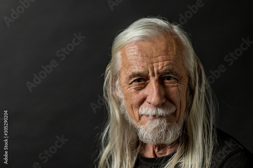 Low key portrait of attractive long gray hair old man looking at camera with tranquility. 