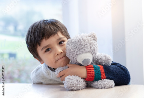 Portrait cute boy laying his head on teddy bear and looking out with beautiful brown eyes, Adorable Child playing with toys and relaxing while waiting for food in cafe.