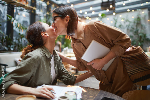 Fotografia Side view portrait of two young women kissing each other on cheek during meeting