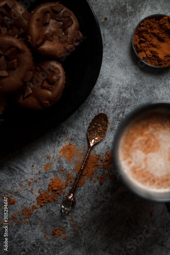 cocoa drink in blue mug with chocolate on dark textured background with chocolate muffins and vintage spoon and cocoa powder.