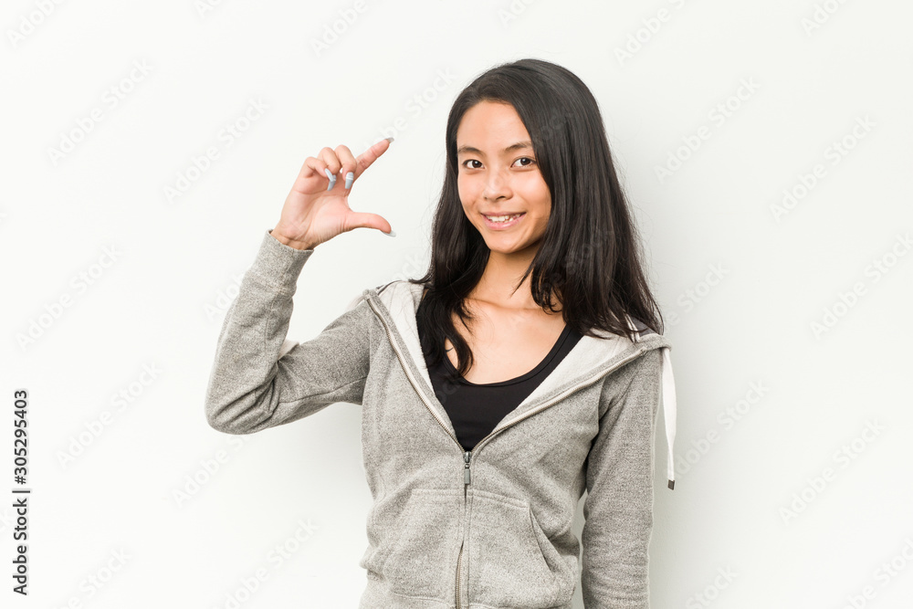 Young fitness chinese woman holding something little with forefingers, smiling and confident. Young fitness chinese woman holding something little with forefingers, smiling and confident.
