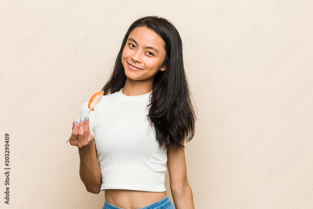Young asian woman holding a sushi piece happy, smiling and cheerful. Young asian woman holding a sushi piece happy, smiling and cheerful.