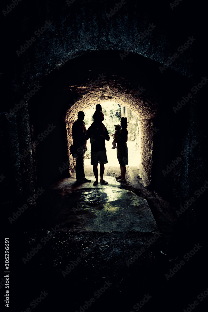 light at end of the tunnel, an artistic monochromatic street photo with a group of people standing in a narrow passage with bright light in the background, old architecture, dark mood, book cover