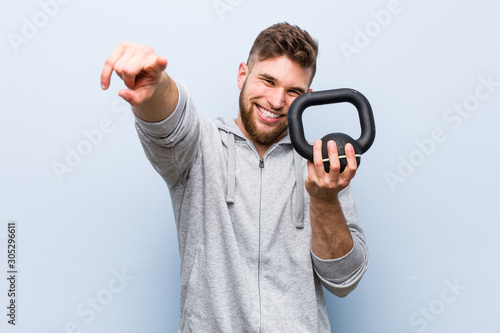Young caucasian sportsman holding a dumbbell cheerful smiles pointing to front.
