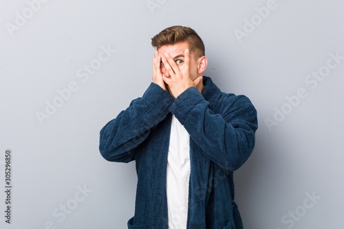 Young caucasian man wearing pajama blink through fingers frightened and nervous.