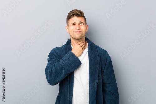 Young caucasian man wearing pajama suffers pain in throat due a virus or infection.