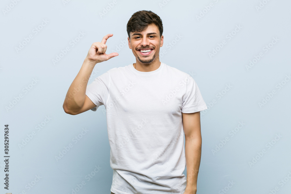 Young caucasian man wearing a white tshirt holding something little with forefingers, smiling and confident. Young caucasian man wearing a white tshirt holding something little with forefingers, smiling and confident.