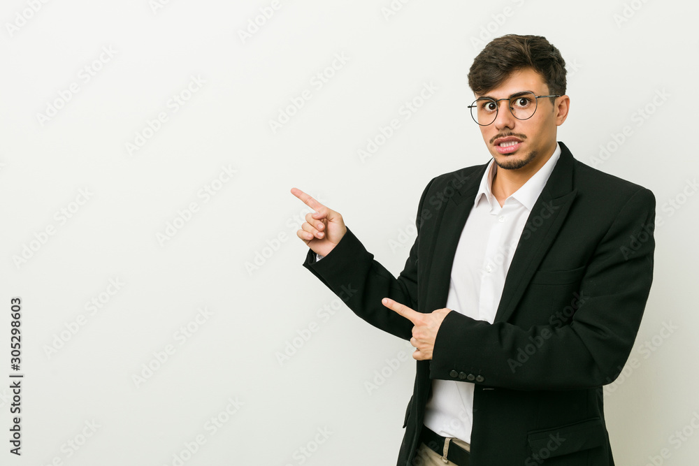 Young business hispanic man shocked pointing with index fingers to a copy space. Young business hispanic man shocked pointing with index fingers to a copy space.