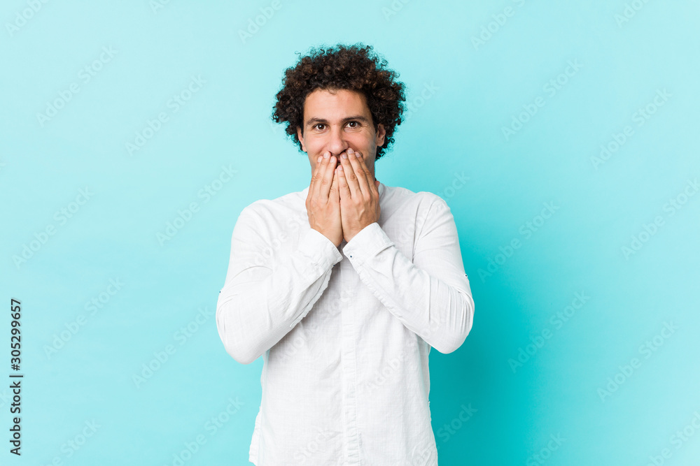 Young curly mature man wearing an elegant shirt laughing about something, covering mouth with hands. Young curly mature man wearing an elegant shirt laughing about something, covering mouth with hands.