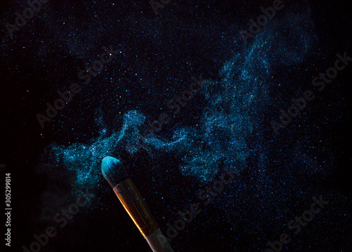 Make-up brush with blue powder explosion isolated on black background