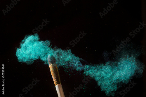 Make-up brush with green powder explosion isolated on black background