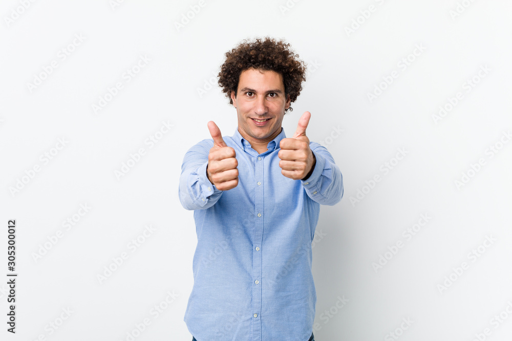 Young curly mature man wearing an elegant shirt with thumbs ups, cheers about something, support and respect concept. Young curly mature man wearing an elegant shirt with thumbs ups, cheers about something, support and respect concept.