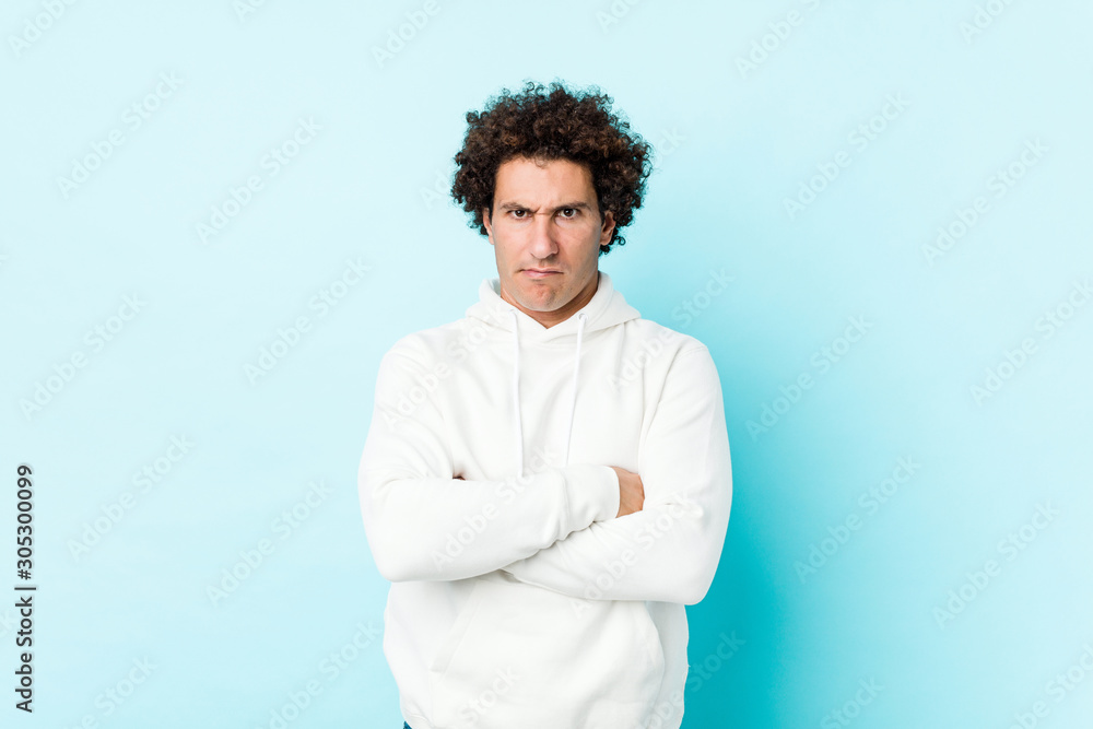 Young sporty man against a blue background frowning face in displeasure, keeps arms folded. Young sporty man against a blue background frowning face in displeasure, keeps arms folded.