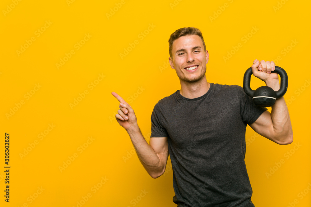 Young caucasian man holding a dumbbell smiling cheerfully pointing with forefinger away. Young caucasian man holding a dumbbell smiling cheerfully pointing with forefinger away.