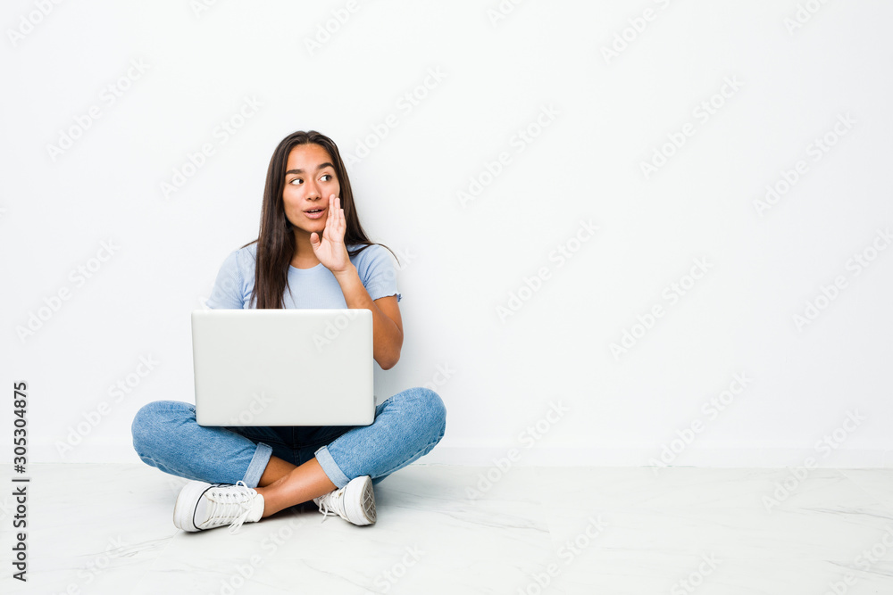 Young mixed race indian woman sitting working on laptop is saying a secret hot braking news and looking aside Young mixed race indian woman sitting working on laptop is saying a secret hot braking news and looking aside