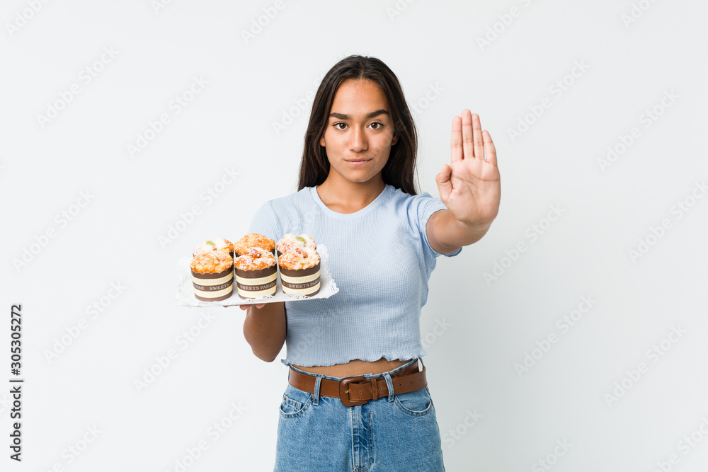 Young mixed race indian holding a sweet cakes standing with outstretched hand showing stop sign, preventing you. Young mixed race indian holding a sweet cakes standing with outstretched hand showing stop sign, preventing you.