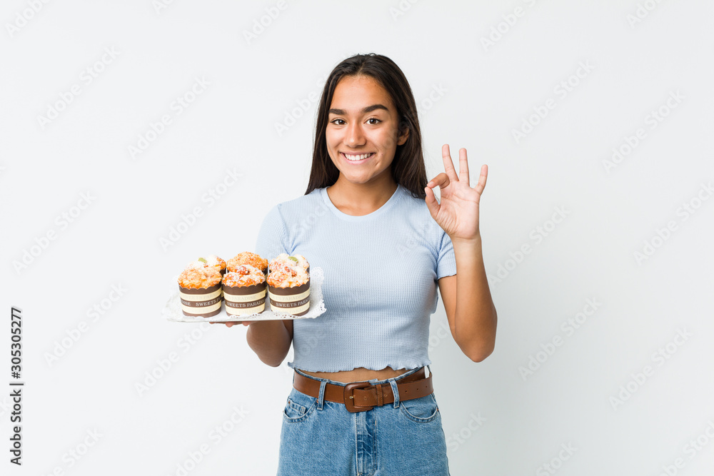 Young mixed race indian holding a sweet cakes cheerful and confident showing ok gesture. Young mixed race indian holding a sweet cakes cheerful and confident showing ok gesture.