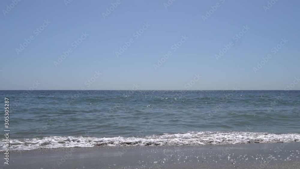 Waves of the pacific ocean beat on the shore in Malibu Beach Los Angeles California. The camera moves over the sand. Steadicam shot. Warm sunny summer day at the beach in Malibu. Waves of the pacific ocean beat on the shore in Malibu Beach Los Angeles California. The camera moves over the sand. Steadicam shot. Warm sunny summer day at the beach in Malibu.